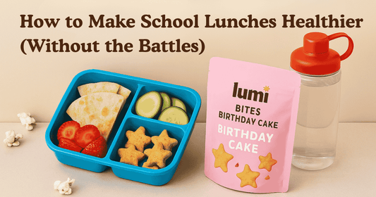 Healthy school lunchbox with Lumi Bites Birthday Cake, fruit, popcorn, crackers, and water bottle on neutral background.